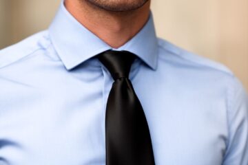 Muž v modré košili a černé hedvábné kravatě na neutrálním rozostřeném pozadí