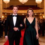 Elegantní pár vstupuje do filharmonie s červeným kobercem, okolí lidé v oblecích a večerních šatech