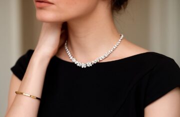 Detail horní části těla ženy v černých šatech s diamantovým náhrdelníkem a zlatým náramkem
